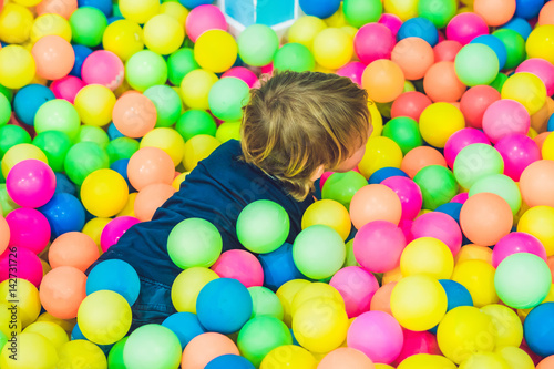 Happy little kid boy playing at colorful plastic balls playground high view. Funny child having fun indoors