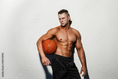 Very muscular naked man holding a basketball in studio photo