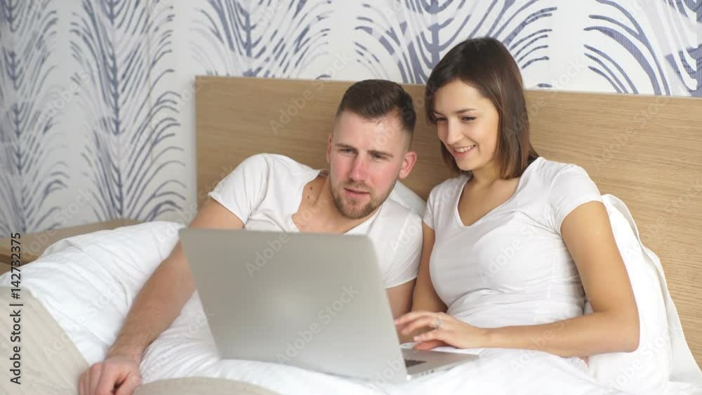 Young couple with laptop watching movie in bed Young couple with laptop watching movie in bed