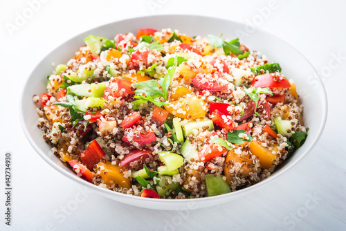 Fresh healthy salad with quinoa, colorful tomatoes, sweet pepper, cucumber and parsley on white wooden background close up. Food and health. Superfood.
