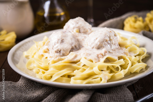 Pasta tagliatelle plate with meatballs and creamy sauce on dark wooden background close up. Italian cuisine. Delicious meal.