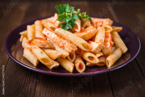 Penne pasta with tomato sauce on dark wooden background top view. Italian cuisine.