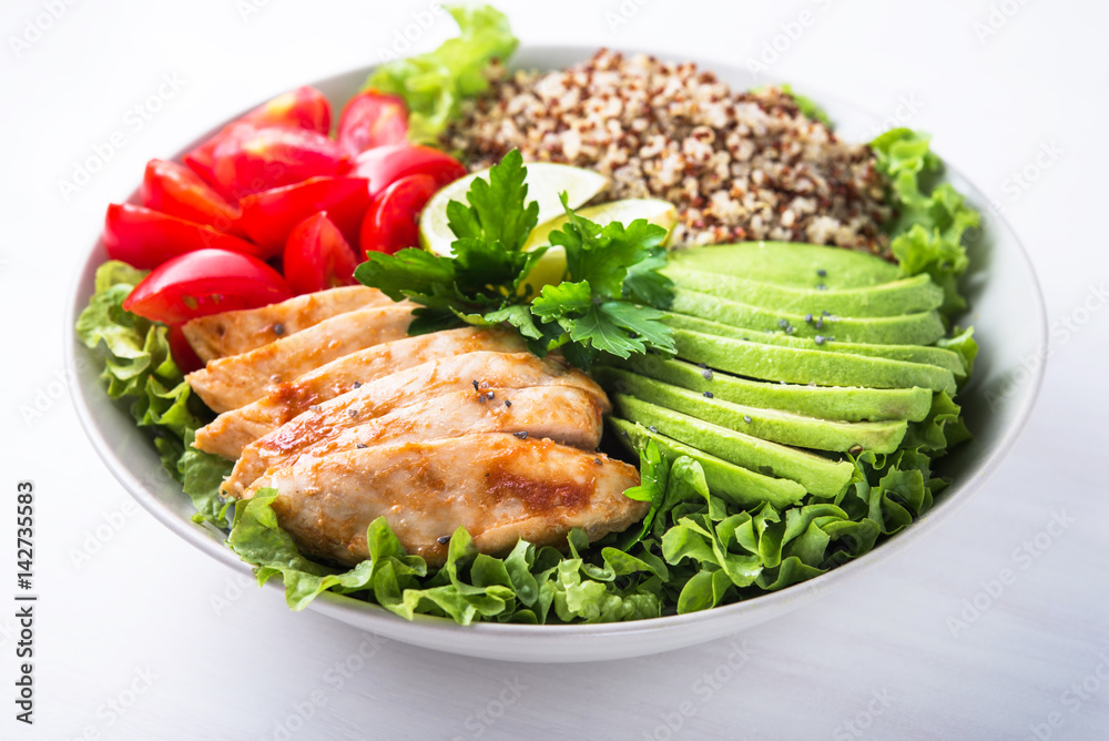 Healthy salad bowl with quinoa, tomatoes, chicken, avocado, lime and mixed greens (lettuce, parsley) on white wooden background close up. Food and health.