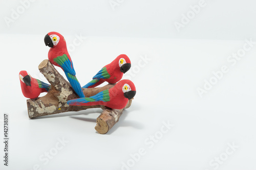 Macaws made in clay seated on a wood branch isolated in white background