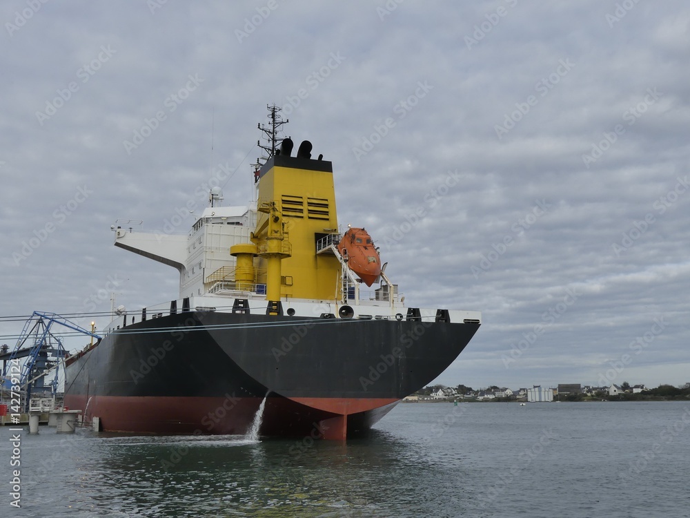 Fototapeta premium Products Tanker discharging at the Oil Terminal of Lorient, France, with black hull and yellow funnel on a cloudy day. Horizontal stern view