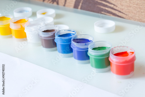 gouache. 8 gouache jars in a row. colorful gouache paint containers.rainbow gouache and piece of white paper