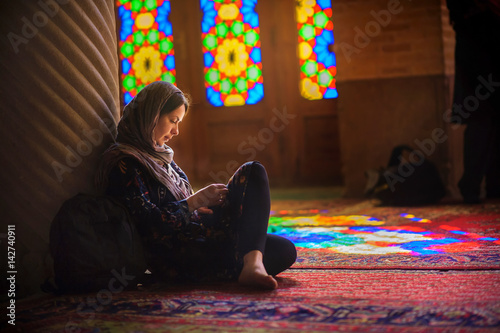 young girl in a scarf sits on a floor in the mosque, is attentive that that reads, bright multi-colored patches of light