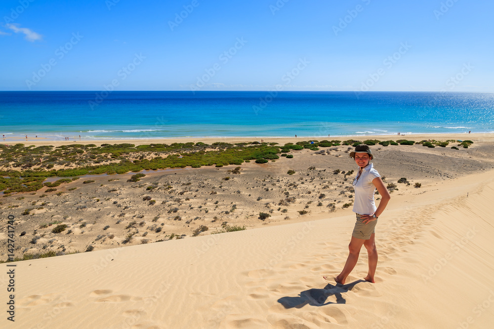 Young woman standing on sand dune on Sotavento beach on Jandia peninsula and looking at ocean, Fuerteventura, Canary Islands, Spain Young woman standing on sand dune on Sotavento beach on Jandia peninsula and looking at ocean, Fuerteventura, Canary Islands, Spain