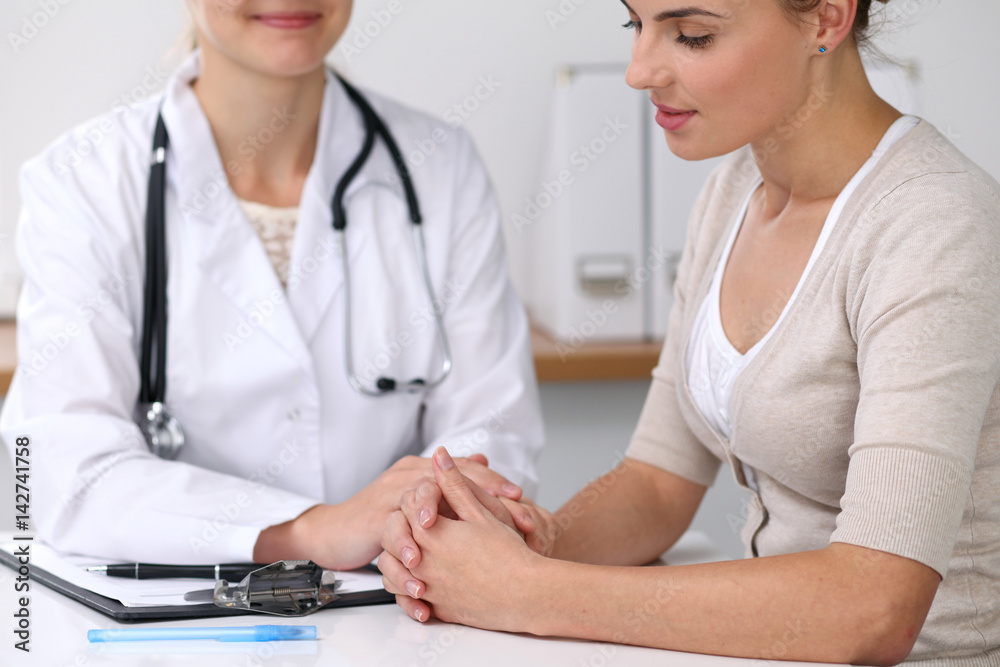 Obraz premium Close up of a doctor reassuring her female patient while sitting at the desk. Medicine, help and health care concept