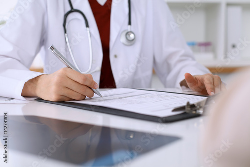 Close up of a female doctor filling up  an application form while consulting patient. Medicine and health care concept