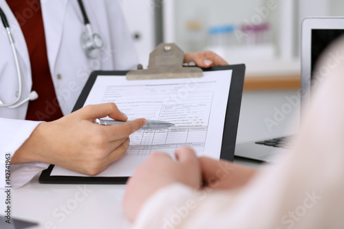 Close up of a female doctor pointing into an application form while consulting patient. Medicine and health care concept