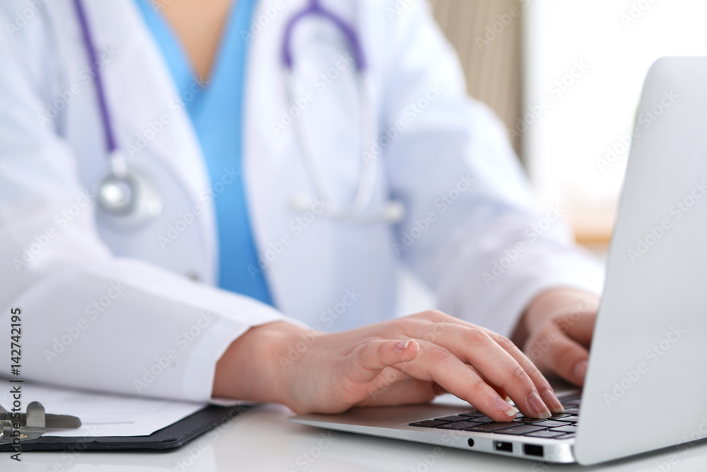 Close up of unknown female doctor typing on laptop computer while sitting at the table. Medical staff, compulsory work concept Close up of unknown female doctor typing on laptop computer while sitting at the table. Medical staff, compulsory work concept