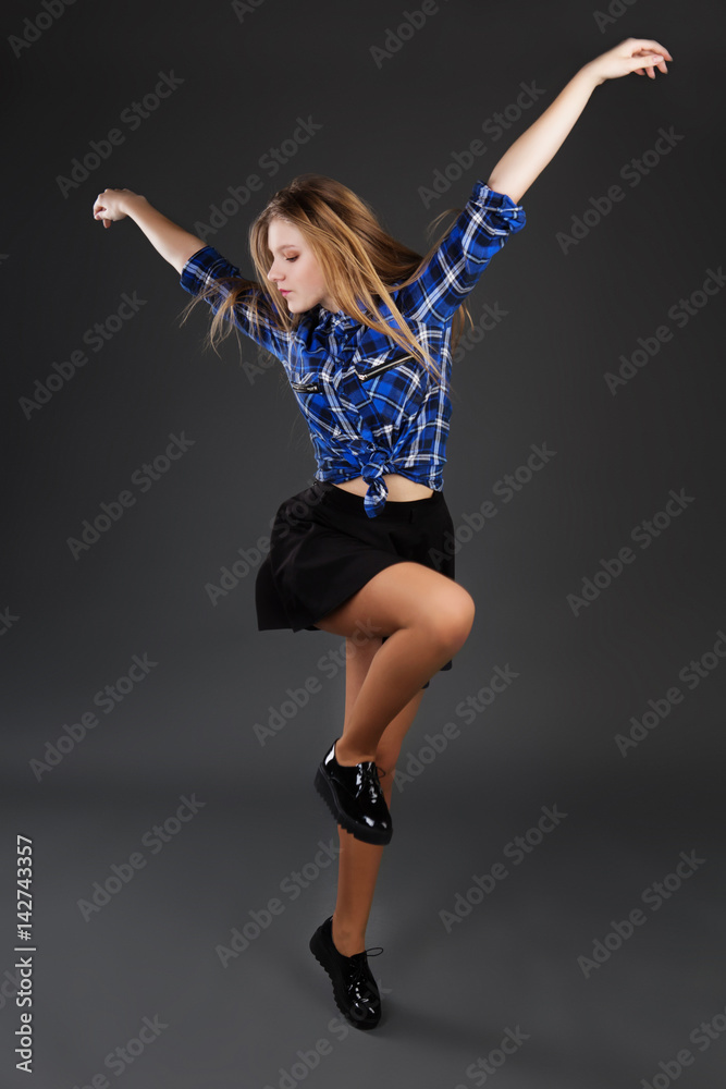 pretty modern slim hip-hop style teenage girl jumping dancing on a dark grey studio background.
