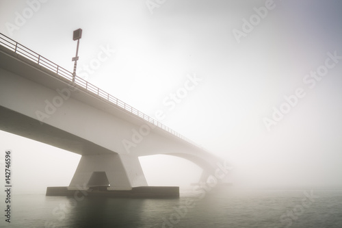 Low visibility due to heavy fog covering the Zeeland bridge, sunshine is visible at the background