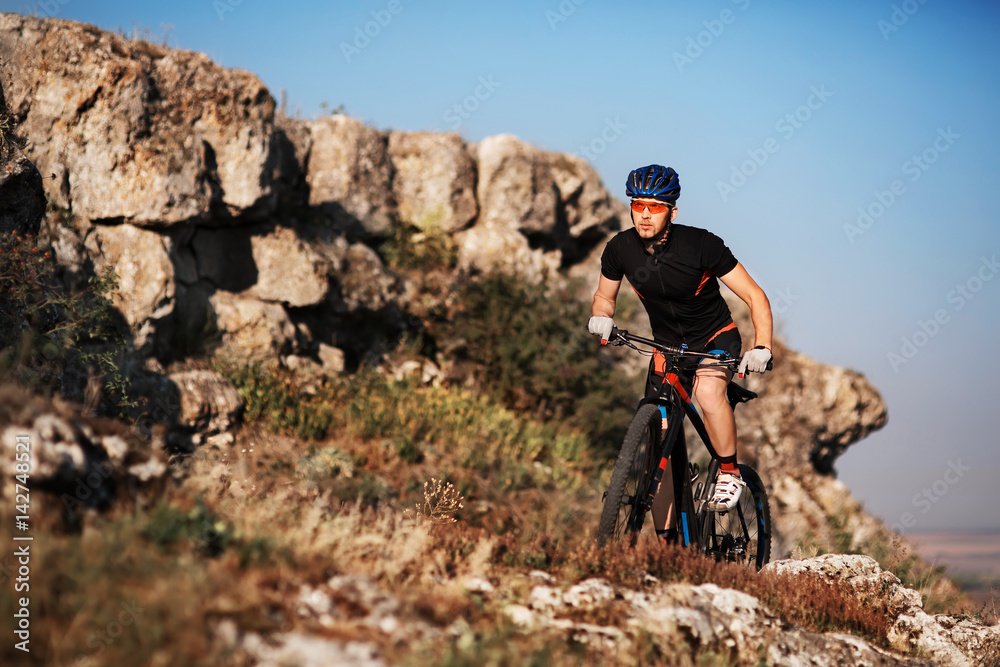 Cyclist in black sportwear Riding the Bike on the Rocky Trail. Extreme Sport Concept. Space for Text.