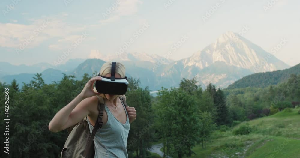 Young woman hiker exploring wilderness mountains wearing virtual reality headset in nature watching 360 travel video imagination concept enjoying summer trekking in Italian Alps