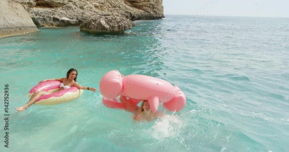 Two girls lying on inflatable flamingo Best friends having fun relaxing floating in clear blue ocean Happy Women enjoying summer vacation on tropical island holiday