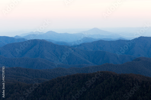 A layered mountain range stretches into the distance under a pastel coloured sunset sky. © Charlie