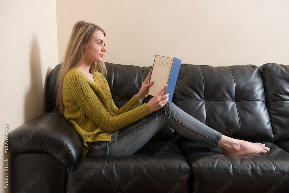 Woman reading a book and sitting on sofa at home Woman reading a book and sitting on sofa at home