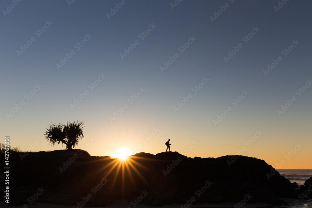 A walking hiker is silhouetted on a ridge line by a beautiful bright sunrise in Australia.