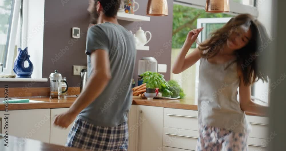 Happy young couple dancing in kitchen wearing pajamas listening to music morning at home having fun Happy young couple dancing in kitchen wearing pajamas listening to music morning at home having fun