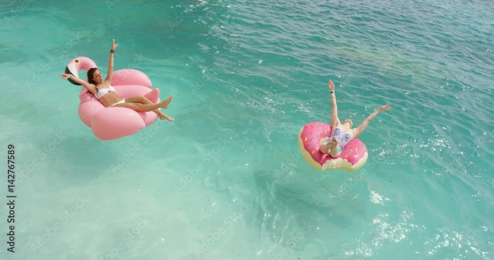 Two girls lying on inflatable flamingo Best friends having fun relaxing floating in clear blue ocean Happy Women enjoying summer vacation on tropical island holiday.