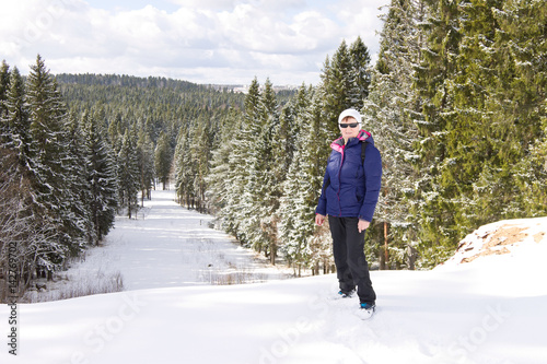 Middle aged female traveler standing on top of a hill against the winter forest background. Northern Russia in winter