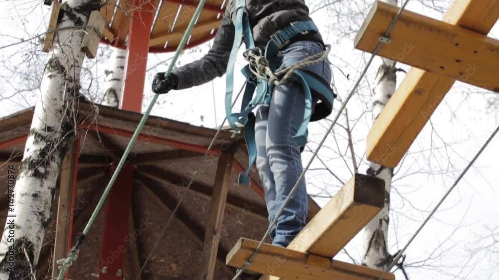 Young female climber walks by pendant log bridge on high ropes course in extreme park. Rock climbing concept. Young female climber walks by pendant log bridge on high ropes course in extreme park. Rock climbing concept.