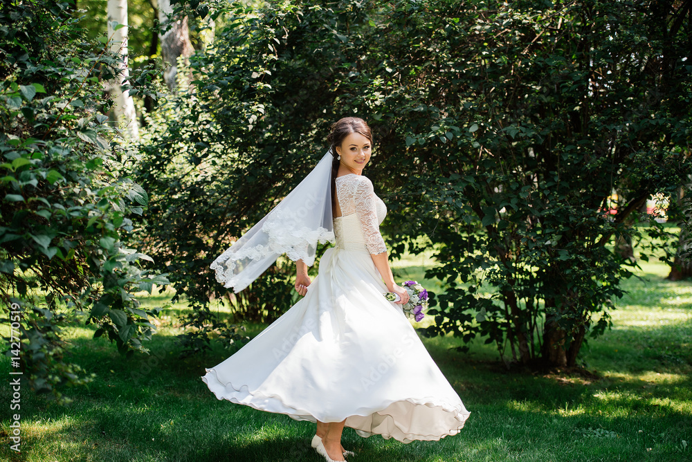 Bride in white dress is spinning in an alley in the park. Dress develops in the wind. Happy bride in a wedding dress is spinning. Bride in white dress is spinning in an alley in the park. Dress develops in the wind. Happy bride in a wedding dress is spinning.