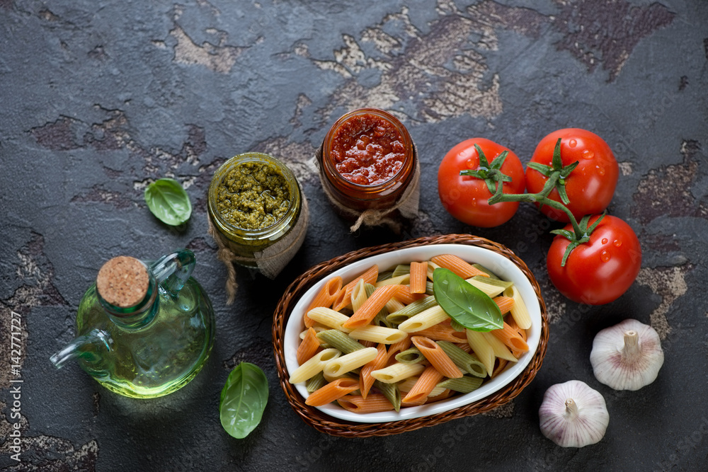 Penne of italian flag colors with red pesto and basil pesto, above view over dark brown stone background