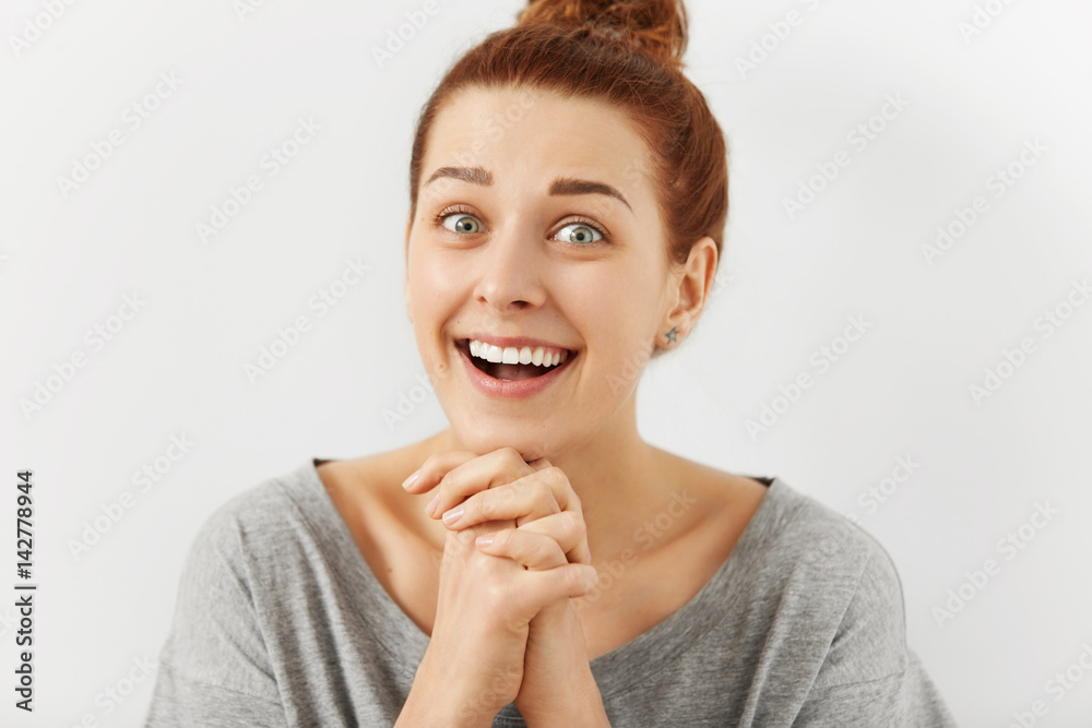 Funny emotional young redhead woman with hairbun keeping hands clasped as if trying to be nice, flattering someone, asking for something. Human facial expressions and emotions. Body language Funny emotional young redhead woman with hairbun keeping hands clasped as if trying to be nice, flattering someone, asking for something. Human facial expressions and emotions. Body language