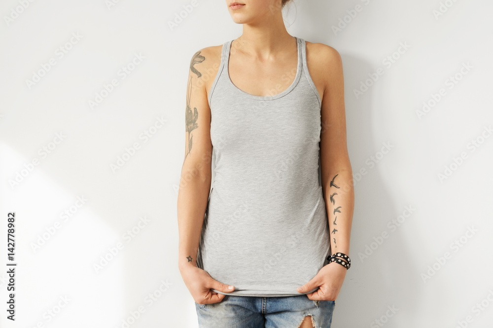 Online shopping. Clothes and apparel. Model posing in blue ripped jeans and  stylish grey tank top with cope space for promotional content. Caucasian  girl with perfect body trying on trendy clothing Stock