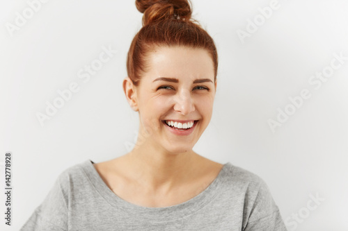 Laughing out loud. Close up shot of attractive cheerful young woman wearing her ginger hair in bun squinting eyes mocking at something funny or ridiculous while relaxing indoors. People and lifestyle