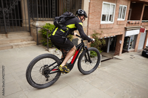Side shot of male cyclist wearing cycling clothing and protective gear speeding on streets riding his pedal-assist electric bike, about to jump down concrete stairs. Exteme sports and adrenaline © wayhome.studio 