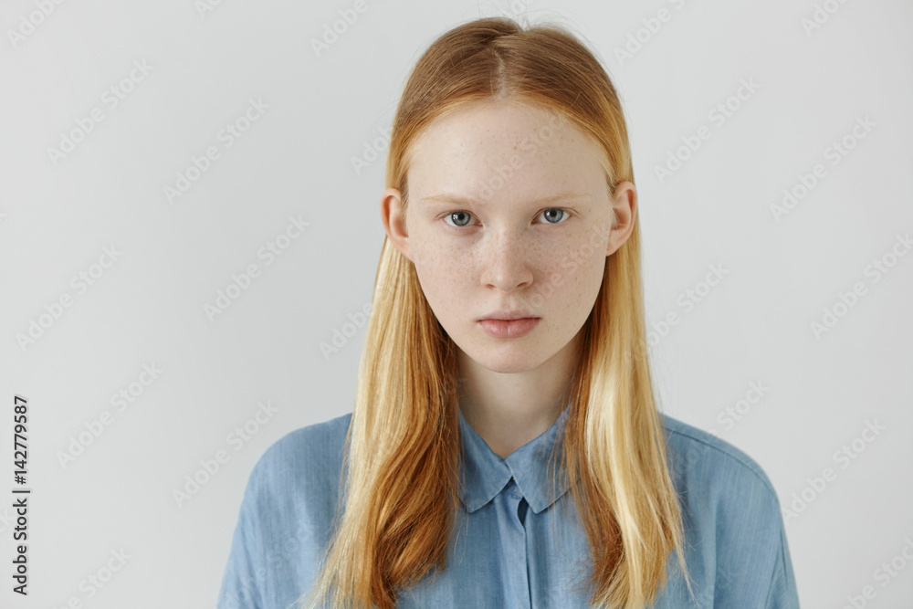 Youth and beauty concept. Portrait of beautiful Caucasian teenage girl wearing her long blonde hair back looking at camera with serious facial expression. Cute young woman with freckles posing indoors Stock Photo | Youth and beauty concept. Portrait of beautiful Caucasian teenage girl wearing her long blonde hair back looking at camera with serious facial expression. Cute young woman with freckles posing indoors Stock Photo |