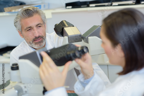 Lab worker holding microscope and talking to colleague