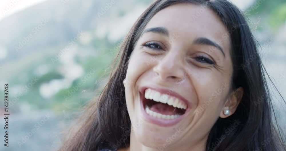 Close up portrait of beautiful young woman smiling hair blowing in wind outdoors slow motion
