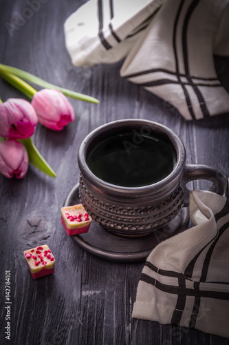 Black coffee, gourmet chocolates with raspberries and pink tulips on a dark background