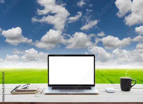 laptop computer showing white screen on work table meadow and blue sky view background