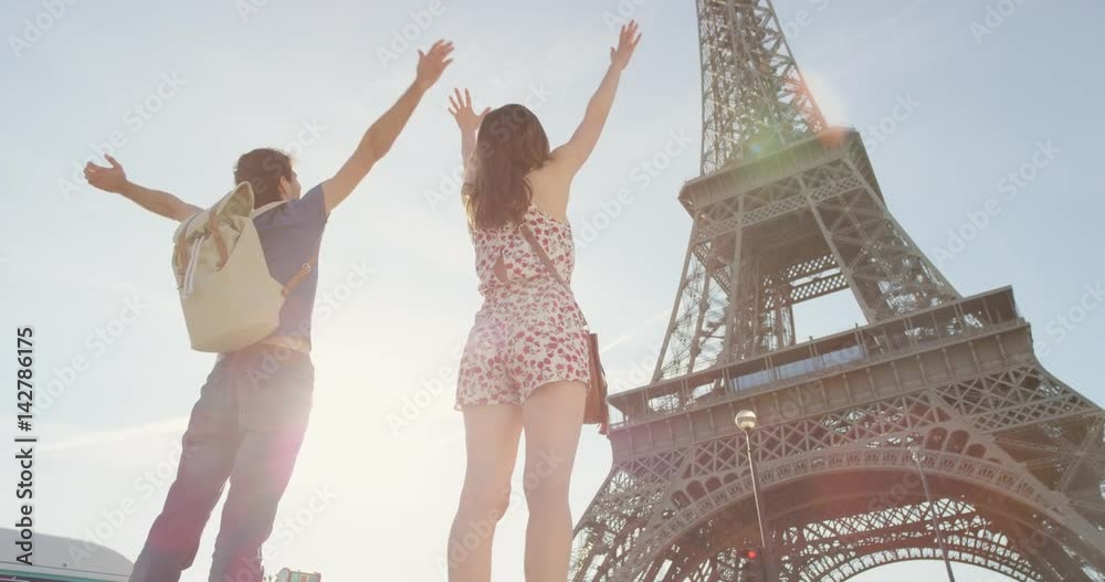 Young tourist couple arms raised looking at Eiffel Tower Paris enjoying european travel adventure celebrating beautiful city sightseeing exploration