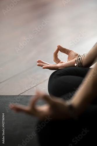 Close up of mudra gesture, performed with female fingers, yogi woman meditating in lotus pose, wearing wrist bracelet, sitting in Padmasana exercise, vertical photo. Meditation session concept