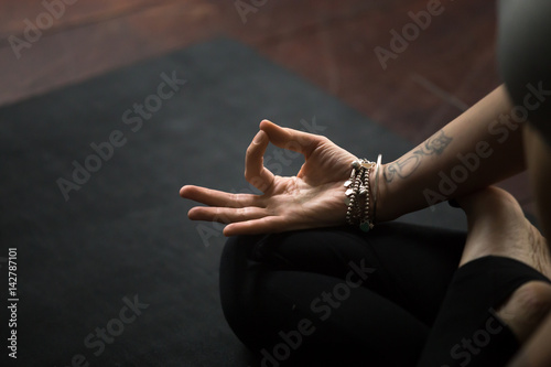 Close up of young woman hand with tattoo and wrist bracelets practicing yoga, sitting in Padmasana exercise on black mat, Lotus pose with mudra gesture, working out, meditating, copy space background photo