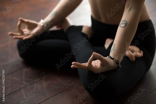 Midsection close up of young yogi woman with tattoo and nice wrist bracelets practicing yoga, sitting in Padmasana exercise, Lotus pose with mudra gesture, working out, wearing black sportswear pants
