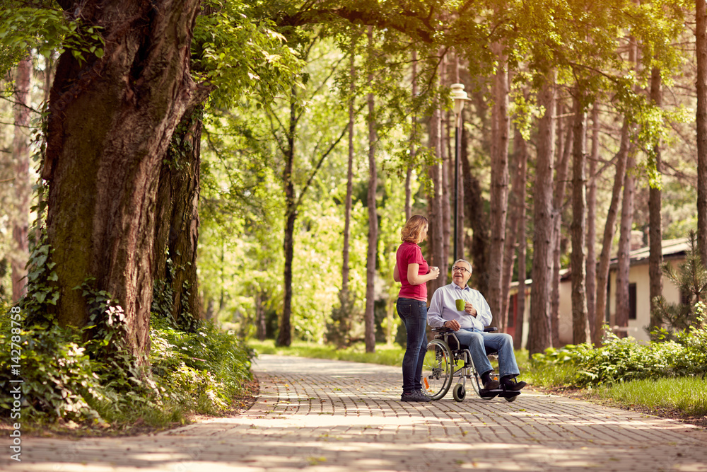 woman visiting her disabled father in wheelchair and enjoying time together in the park. woman visiting her disabled father in wheelchair and enjoying time together in the park.