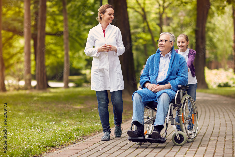 elderly man on wheelchair with nurse and granddaughter outdoor. elderly man on wheelchair with nurse and granddaughter outdoor.