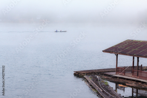 Floating wooden raft house on river with foggy and long tail boat on background.