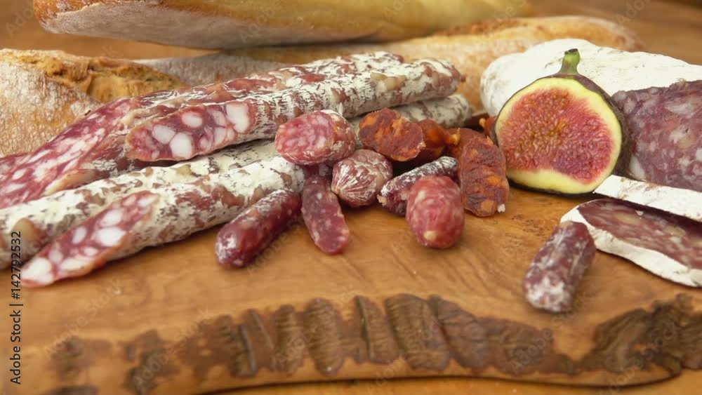 Circular movement of the camera around uncooked jerked sausages, baguette and figs on a wooden board Circular movement of the camera around uncooked jerked sausages, baguette and figs on a wooden board