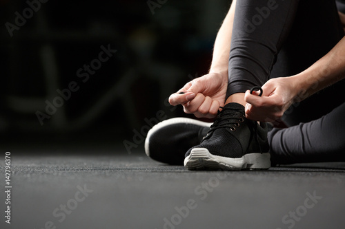 Cropped image of young fitness lady tie laces in gym.