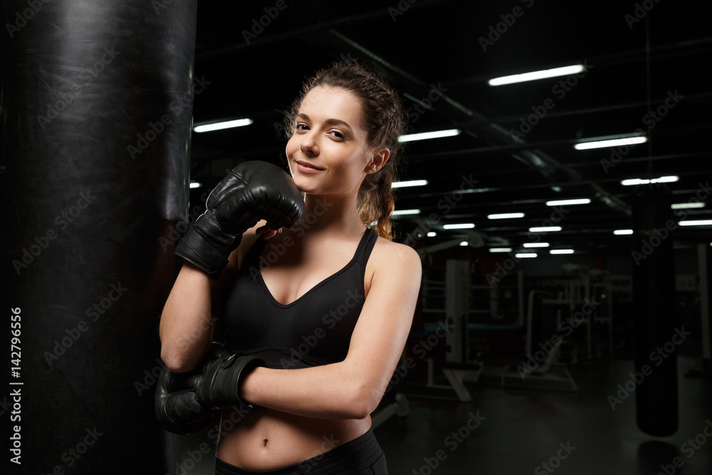 Smiling young strong sports lady boxer standing in gym
