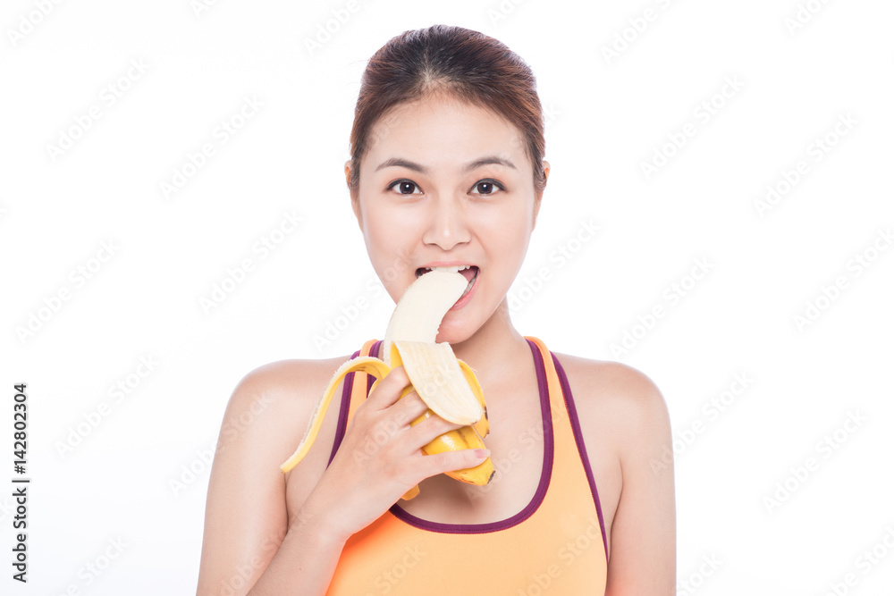 Smiling sporty asian woman holding banana over white background and looking at camera Smiling sporty asian woman holding banana over white background and looking at camera